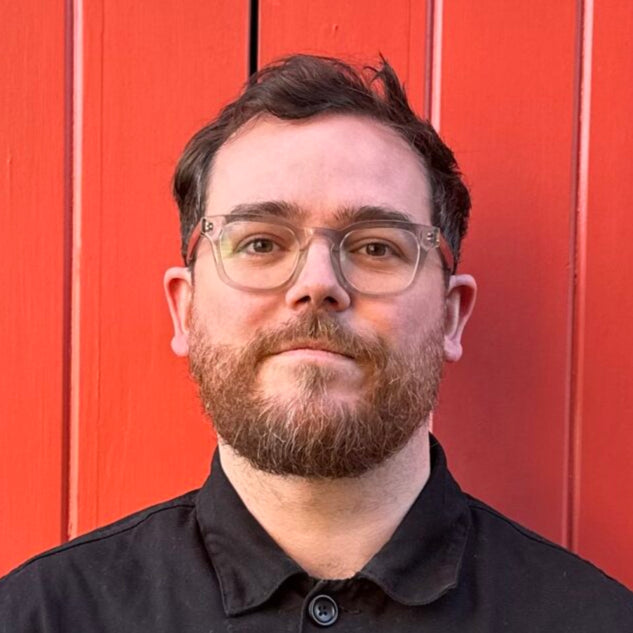 Man wearing a black jacket standing against a red wall.