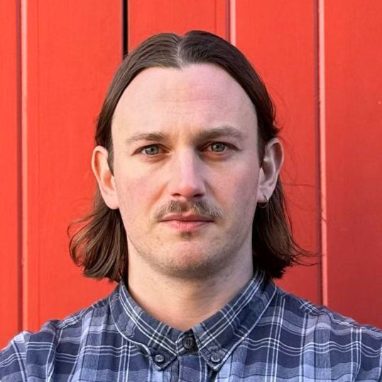 Man wearing a plaid shirt standing against a red wall