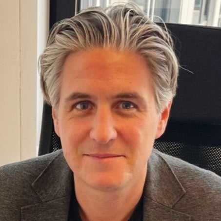 Man sitting in an office chair wearing a gray blazer and black shirt.